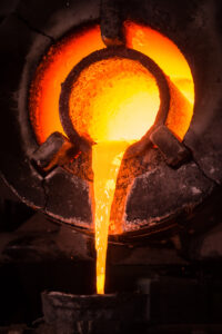 Molten metal pouring from a high-temperature industrial furnace into a casting mold